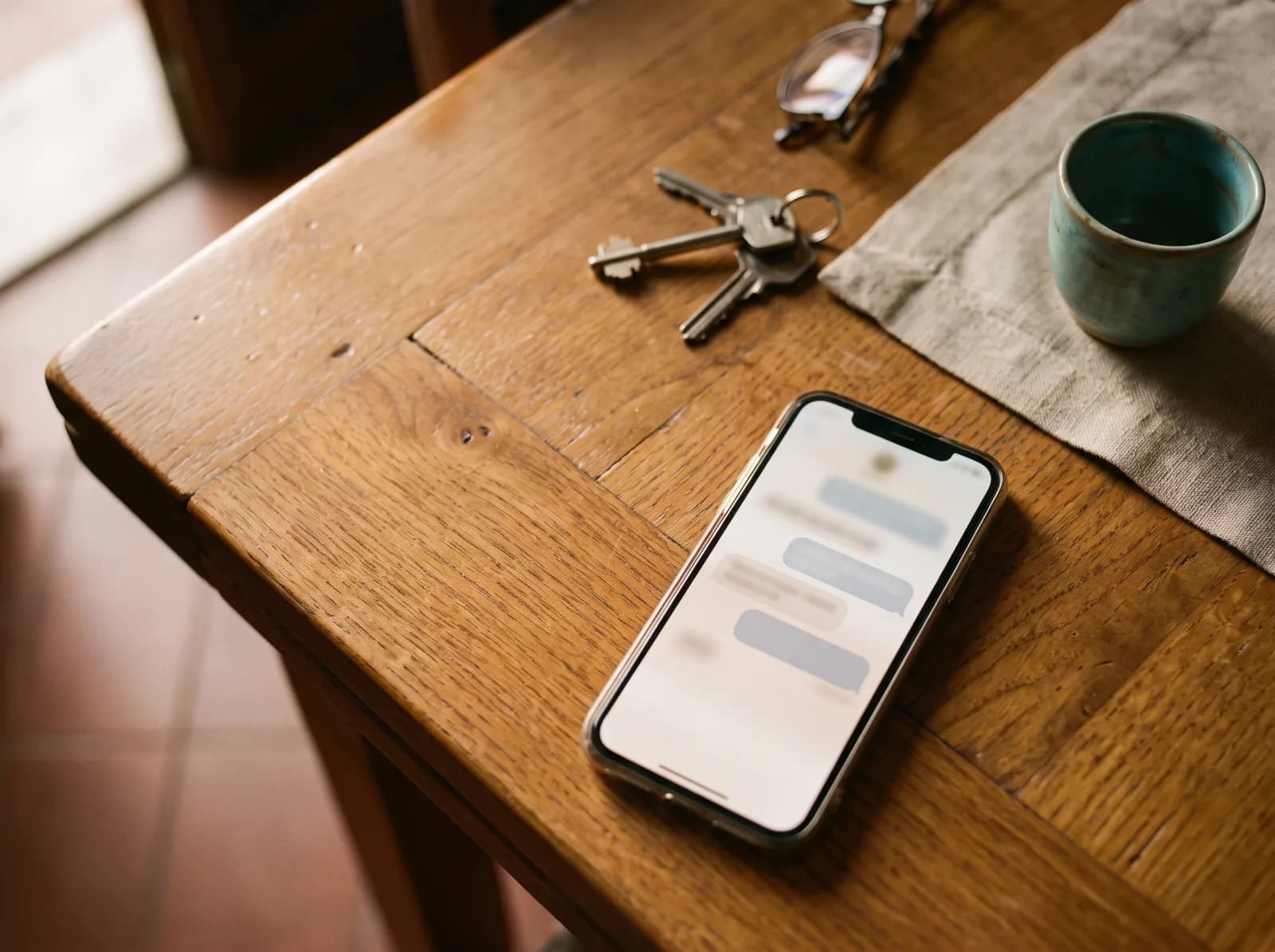 Visto dall’alto: il telefono posato sul tavolo di casa a inizio serata, la conversazione aperta a schermo — il messaggio arriva nella chat che il cliente ha già col salone