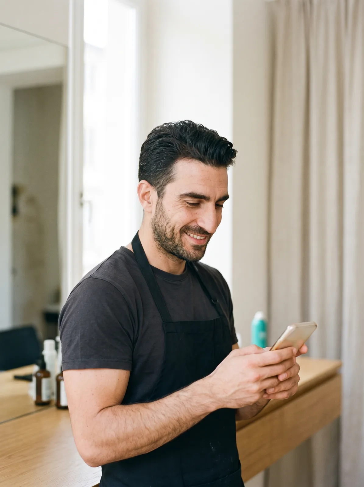 Il titolare del salone che sorride mentre manda un promemoria dal telefono